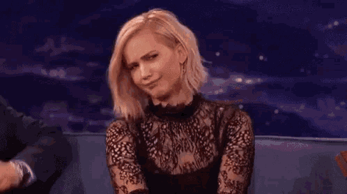 a woman is sitting on a couch wearing a black lace top and making a funny face .