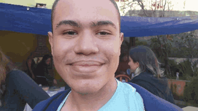 a man in a blue shirt smiles in front of a blue tarp