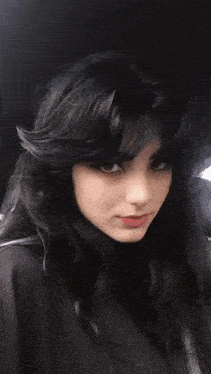 a woman with long black hair is sitting in a car and making a face .