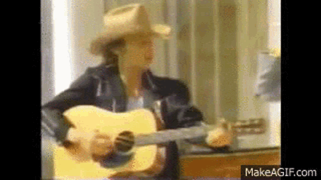 a man wearing a cowboy hat is playing an acoustic guitar .