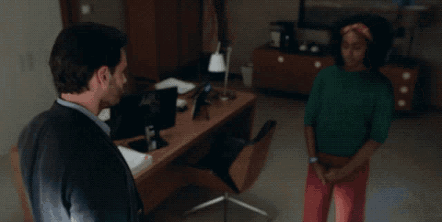 a man is talking to a woman who is standing next to a desk