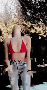 a woman in a red bikini top and ripped jeans is dancing in front of a crowd .