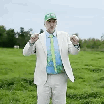 a man in a suit and tie is standing in a grassy field and making a funny face .