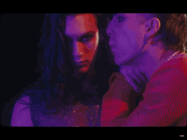 a man and a woman are standing next to each other in a dark room with purple lights behind them