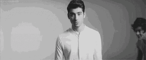 a black and white photo of a young man in a white shirt standing in front of a wall .