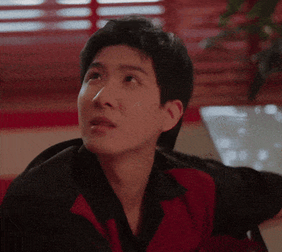 a man in a red and black shirt is sitting at a table looking up .