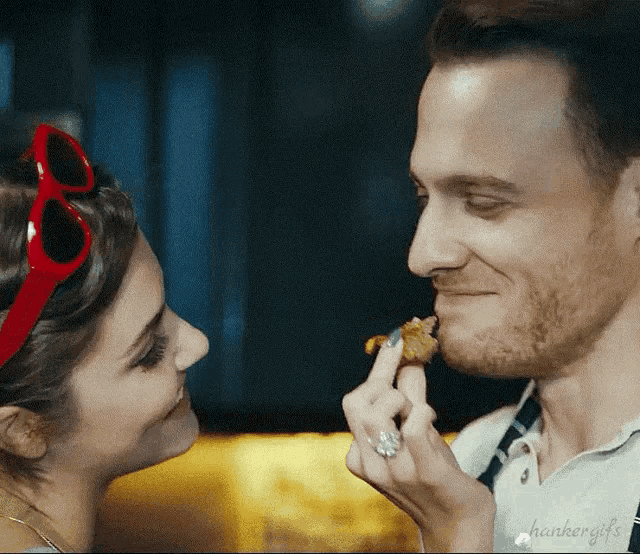 a man is feeding a piece of food to a woman who is wearing red sunglasses ..