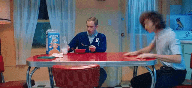 a man is sitting at a table eating cereal and a box of cereal with a bear on it .