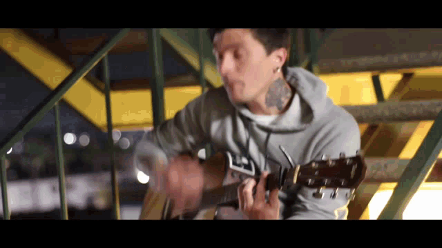 a man in a grey hoodie is playing a guitar on a set of stairs