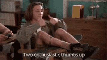 a man is sitting on a table with his legs crossed and a caption that says two enthusiastic thumbs up .