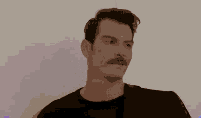a man with a mustache wearing a black shirt and a red jacket is standing in front of a white wall .