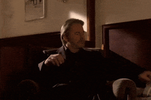 a man with a beard is sitting on a couch with his hands on his chin
