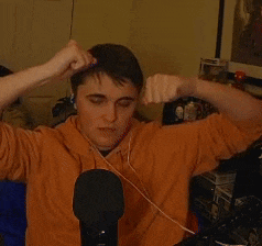a man in an orange shirt is sitting in front of a microphone with his hands on his face
