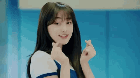 a young woman is making a heart shape with her hands and smiling .