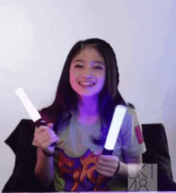 a girl is smiling while holding two glow in the dark lights .