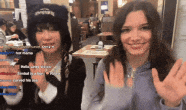 two girls are waving their hands in a restaurant and one of them is wearing a hat that says hello letty vision