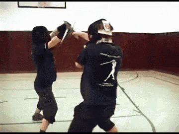 a man wearing a black shirt with a baseball player on the back is fighting another man in a gym .