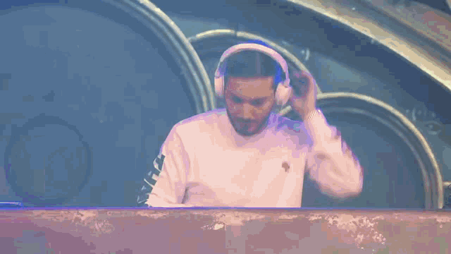 a man wearing headphones and a white shirt with a bird on it stands in front of a clock