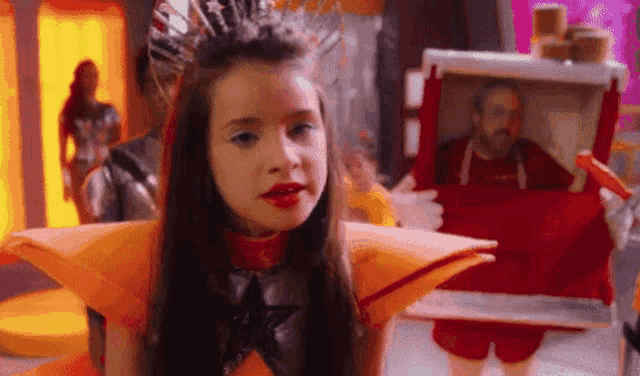 a little girl is wearing a crown and holding a picture of a man in a red box .