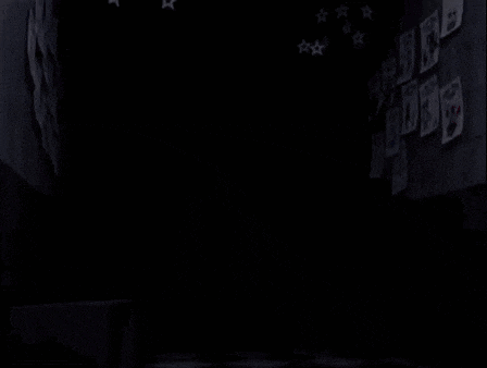 a blue teddy bear with a red bow tie is standing in the dark .