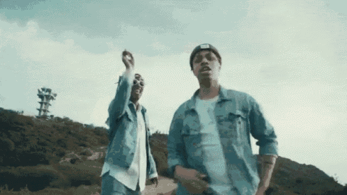 two men in denim jackets are standing next to each other on a hill .