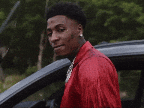 a young man in a red shirt is standing in front of a car