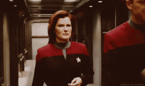 a woman in a star trek uniform is walking down a hallway .