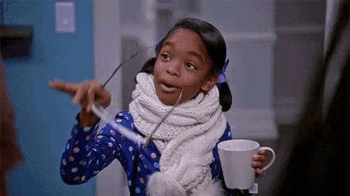 a little girl is wearing a scarf and holding a cup of hot chocolate and a pair of glasses .
