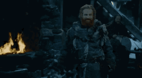a man with a beard is standing in front of a fire and smiling .