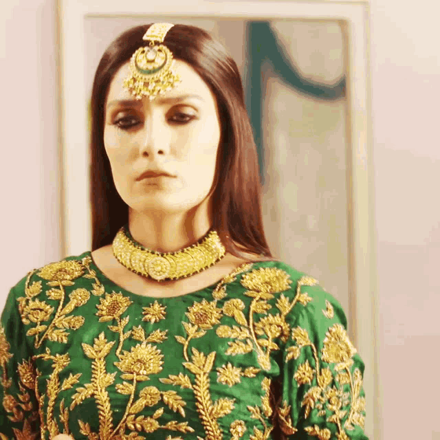 a woman wearing a green top and gold embroidery looks at the camera