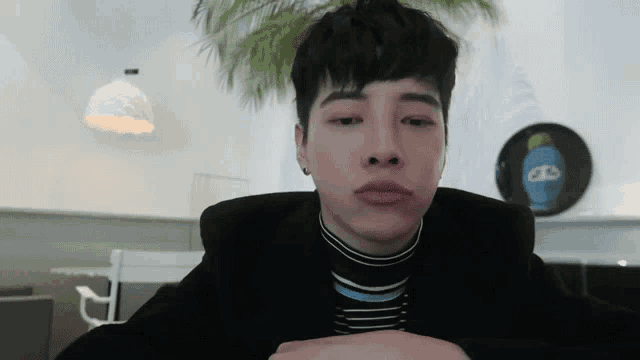 a young man wearing a black jacket and a striped shirt is making a face .