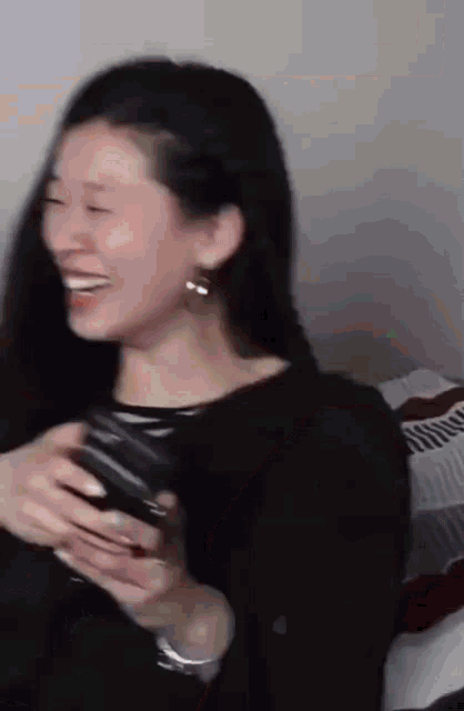 a woman in a black shirt is laughing and holding a glass of wine