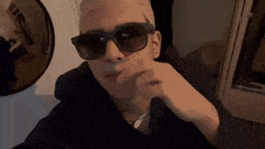 a man wearing sunglasses and a hat is pointing to the camera