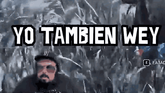 a man wearing sunglasses and a hat is standing in front of a wall that says yo tambien wey