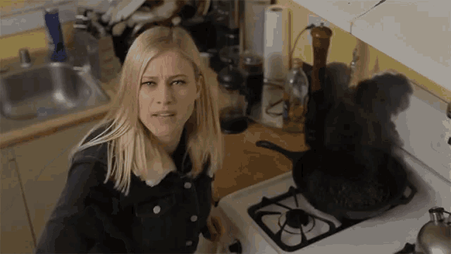 a woman is standing in front of a stove with smoke coming out of it and making a funny face .