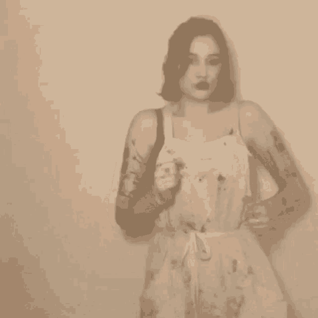 a woman in a white dress is standing in front of a wall and making a funny face .