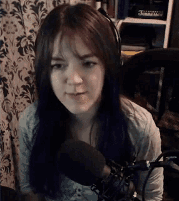a woman wearing headphones is sitting in front of a microphone and looking at the camera .