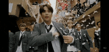 a group of young men in suits and ties are standing in front of a building with confetti falling from the ceiling .