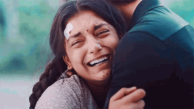 a woman with a bandage on her forehead is laughing while hugging a man .