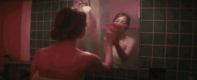 a woman wrapped in a towel is looking at herself in a mirror .