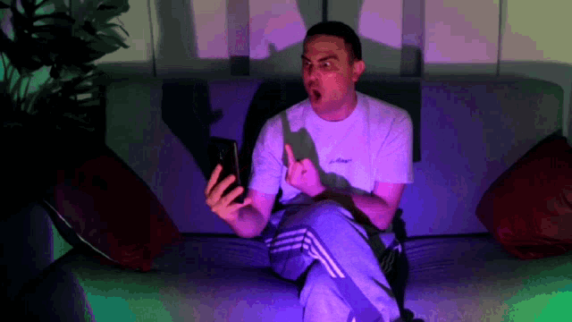 a man is sitting on a couch looking at his phone and making a funny face