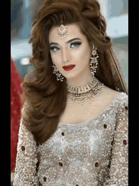 a woman in a silver dress and jewelry is wearing a necklace and earrings .