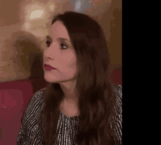 a woman with long hair and red lipstick is sitting on a red couch .