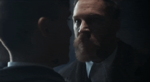 a man with a beard is talking to another man in a dark room .