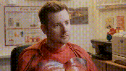 a man in a red shirt is sitting in a chair in front of a computer .