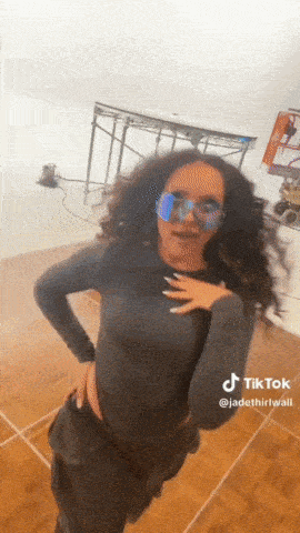 a woman wearing sunglasses and a black top is dancing on a dance floor ..
