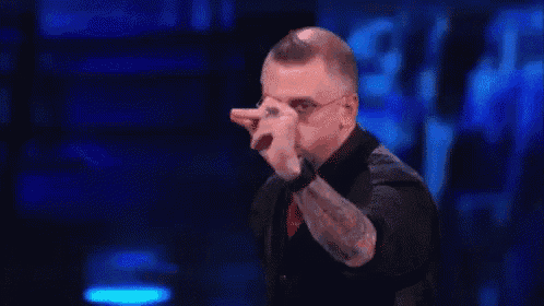 a man wearing glasses and a tattoo is pointing at the camera .
