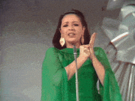 a woman singing into a microphone wearing a green cape