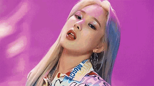 a close up of a woman 's face on a purple background . she is wearing a colorful shirt and earrings .