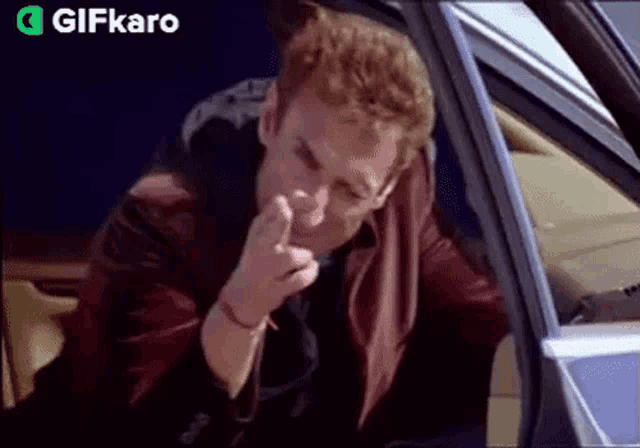 a man is sitting in a car smoking a cigarette and making a funny face .